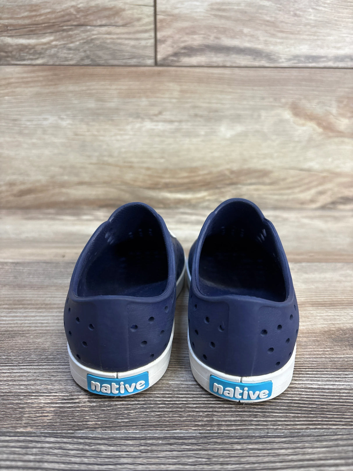 Navy blue Native kids slip-on shoes with white soles on wooden floor