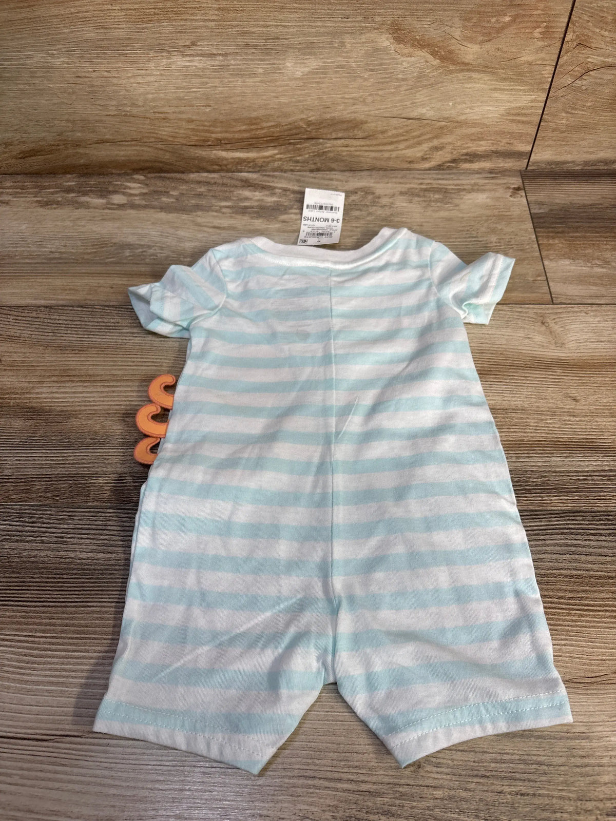 Flat lay of white First Impressions octopus romper with light blue stripes, short sleeves, and octopus graphic on wood surface