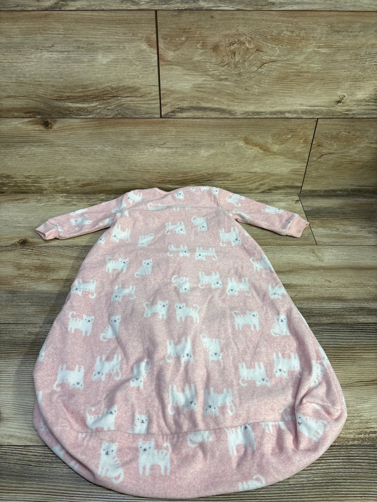 Top-down view of pink baby sleep sack showcasing white cat print, long sleeves, and rounded gathered bottom on wooden floor