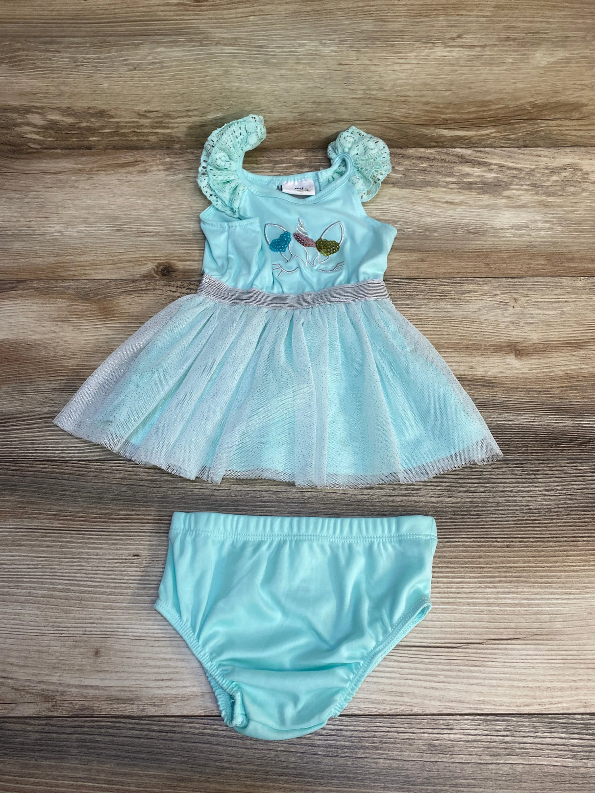 Flat lay of light blue My Destiny 2pc dress and bloomers with sequined unicorn applique and tulle skirt on wood background