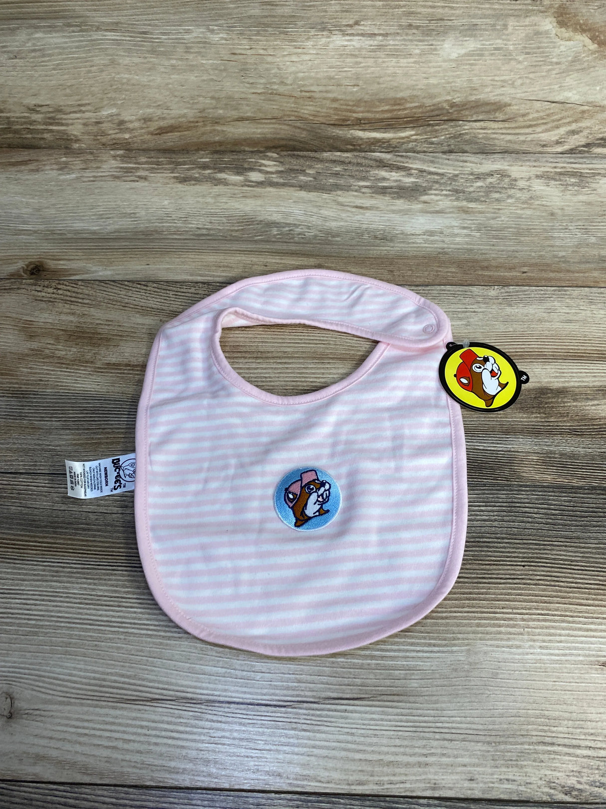 Pink and white striped baby bib with cartoon dog patch and attached tag on wooden surface