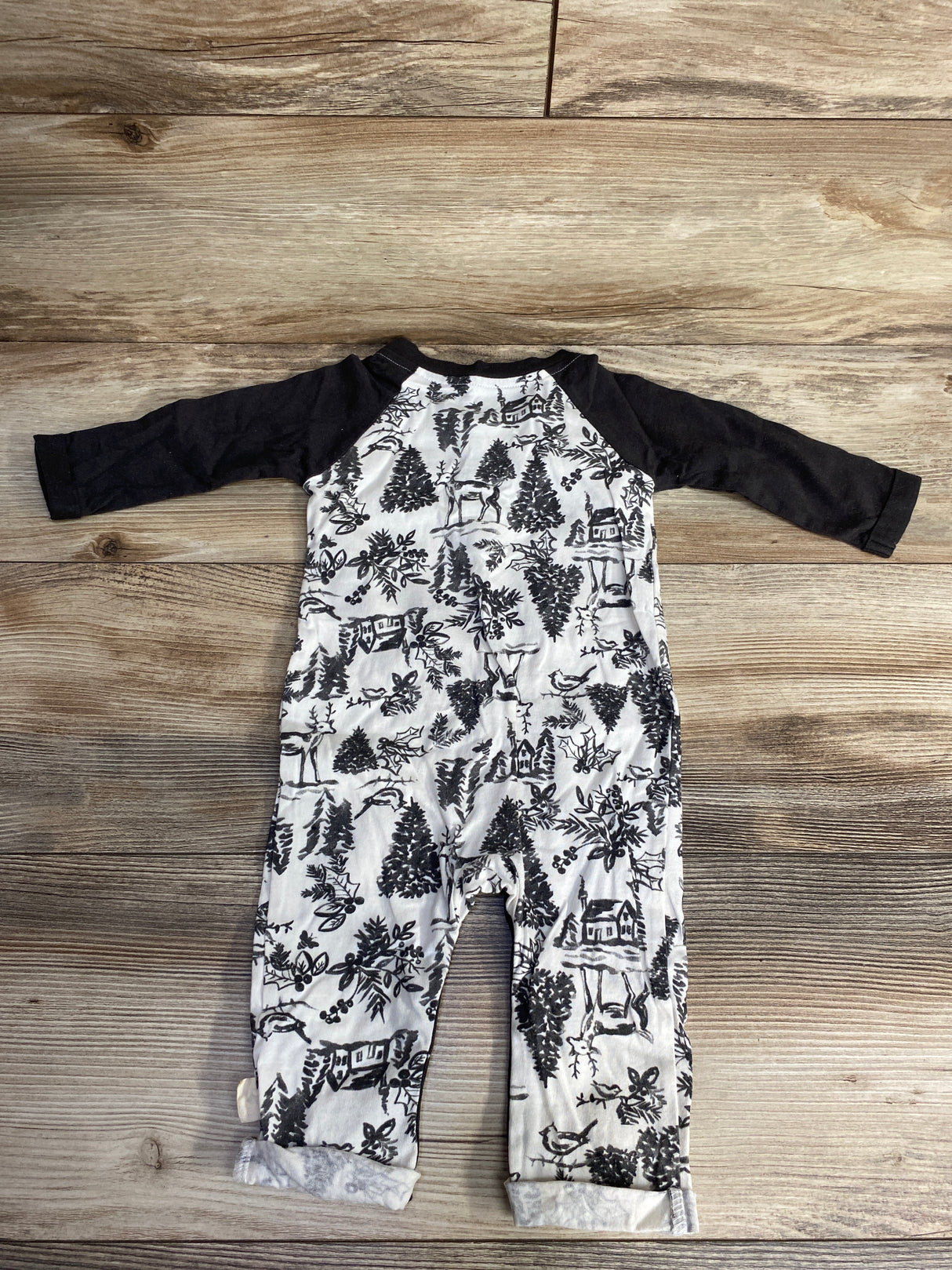 Black and white baby romper with forest and animal print, laid on wooden floor