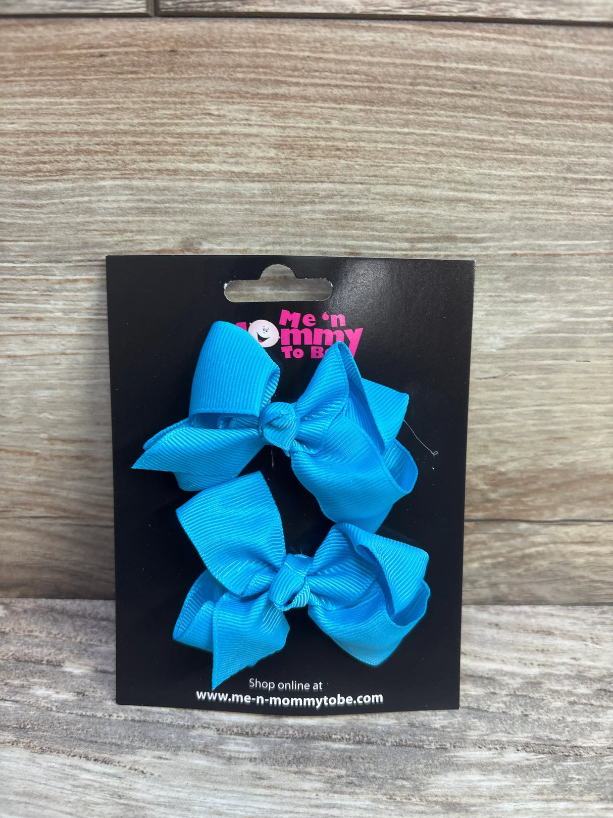Front view of two bright blue grosgrain hair bows 2-pack showing knotted centers on a black branded card against wood background