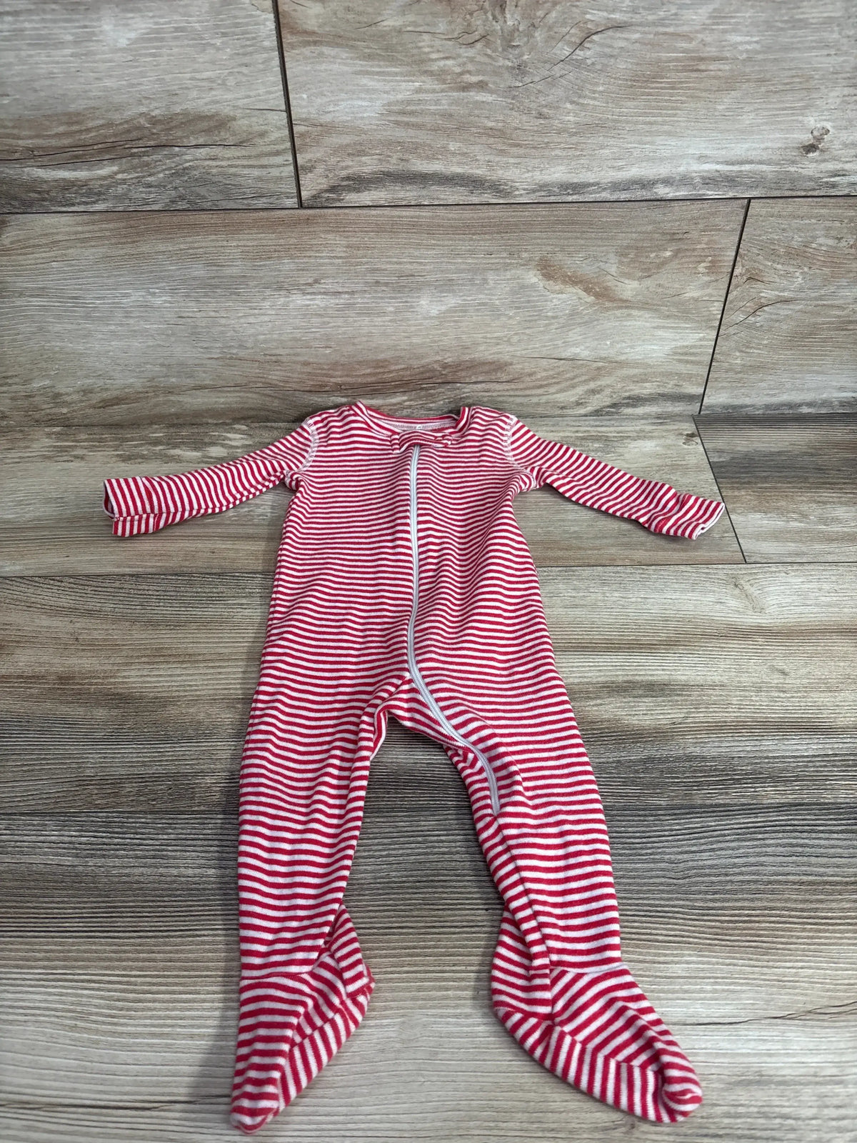 Front flat lay of red and white striped organic footed sleeper showing center zipper and built-in feet on a wood floor background