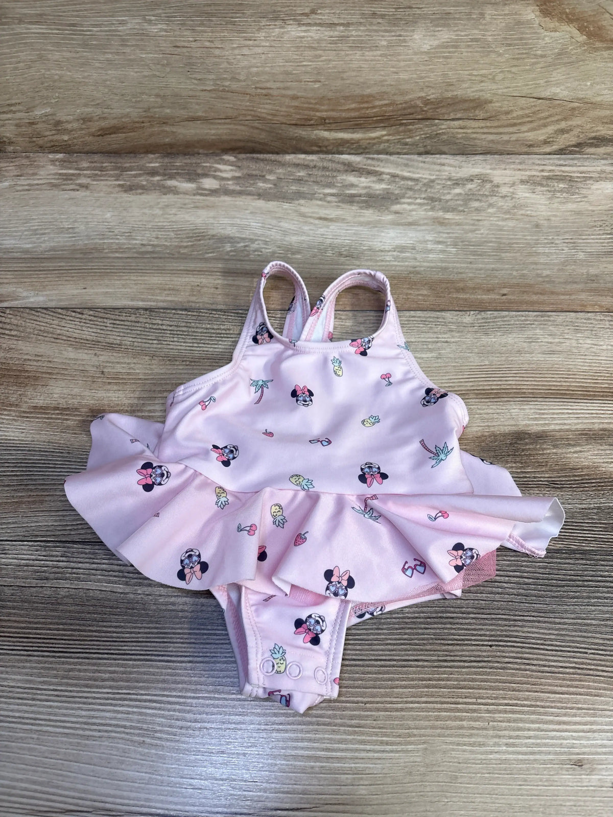 Front view of a pink Minnie Mouse one-piece tutu swimsuit showcasing its twirly skirt and patterned fabric on a wood-grain background