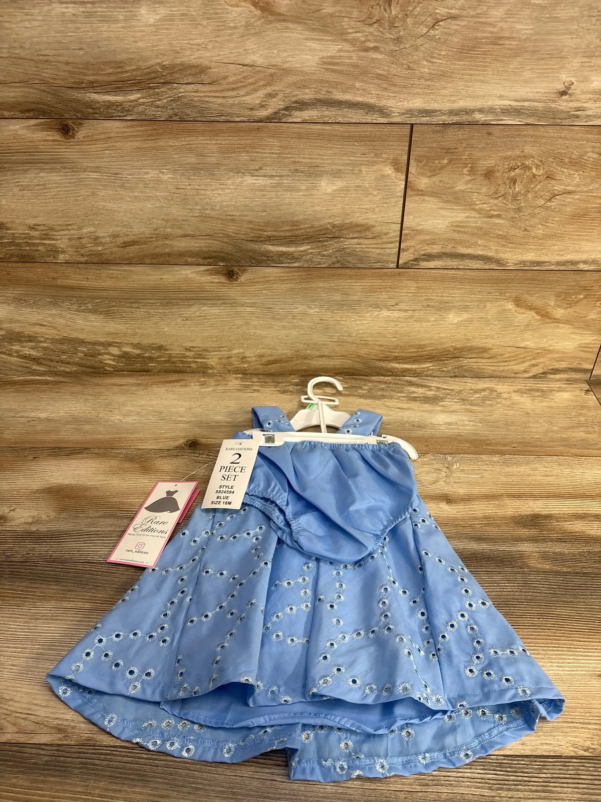 Front flat-lay of blue Rare Editions eyelet dress with matching bloomers on a small hanger showing eyelet embroidery and tags on wood background