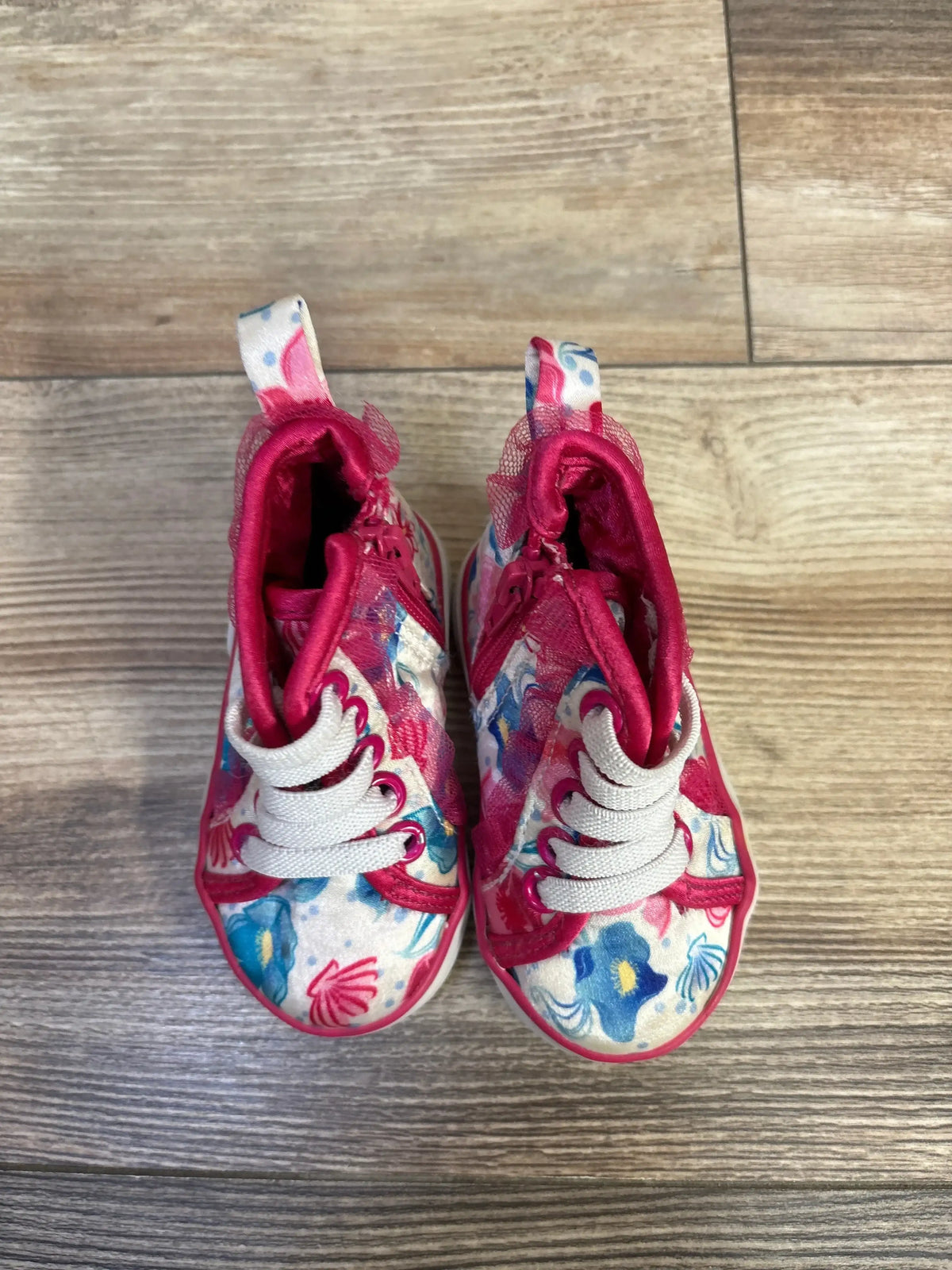 Top-down view of toddler Disney floral high-top sneakers with white laces, pink trim, tulle ankle ruffle on wood floor