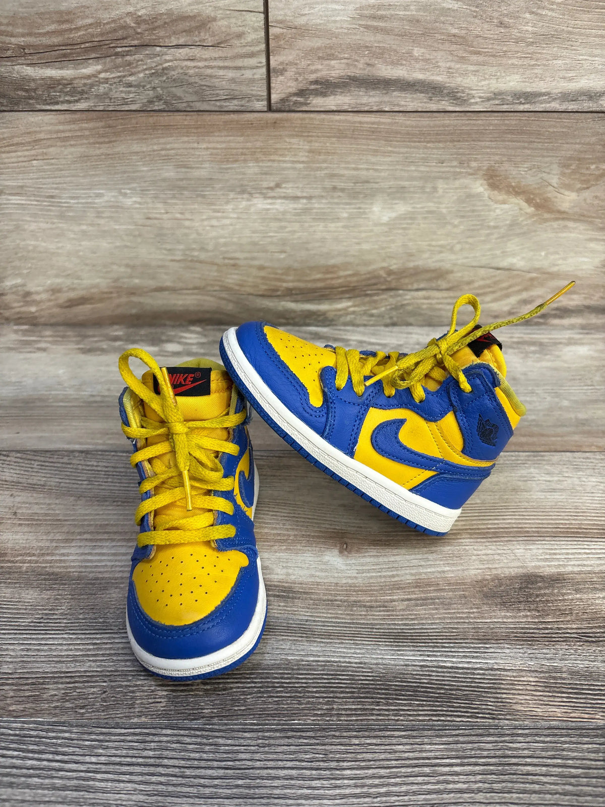 Front and side views of Reverse Laney Air Jordan 1 TD sneakers in Varsity Maize and Game Royal leather on wood flooring