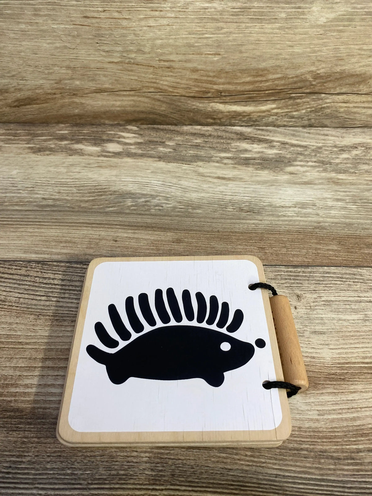 Top-down view of Lovevery wooden board book showing black hedgehog silhouette on white cover and wooden handle on light wood background