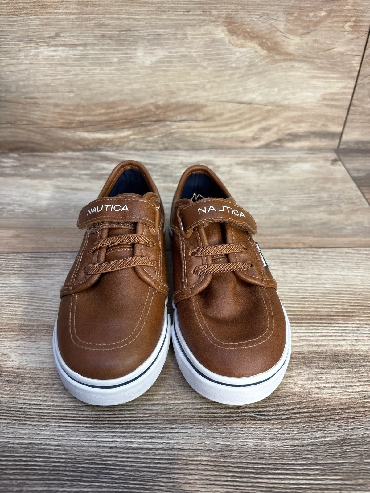 Front view of Nautica Calloway brown faux leather sneakers with lace and strap details, white soles, on a wood-look floor