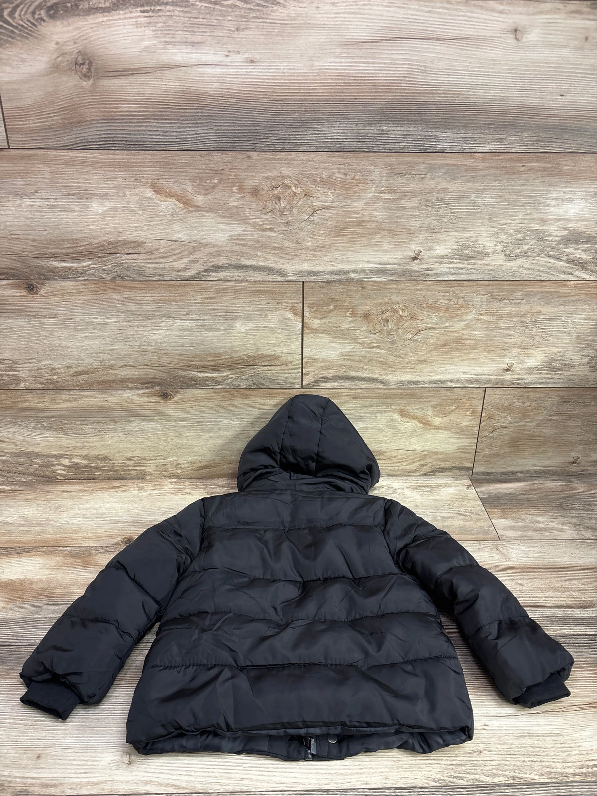 Back view of a black puffer jacket for toddlers by Me n Mommy To Be on a wood background