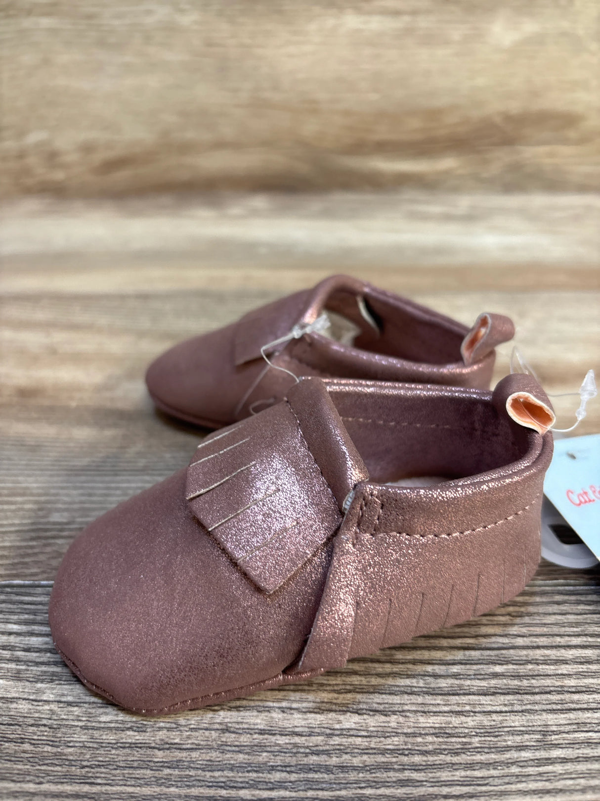 Metallic pink baby moccasins with fringe detail on wooden surface