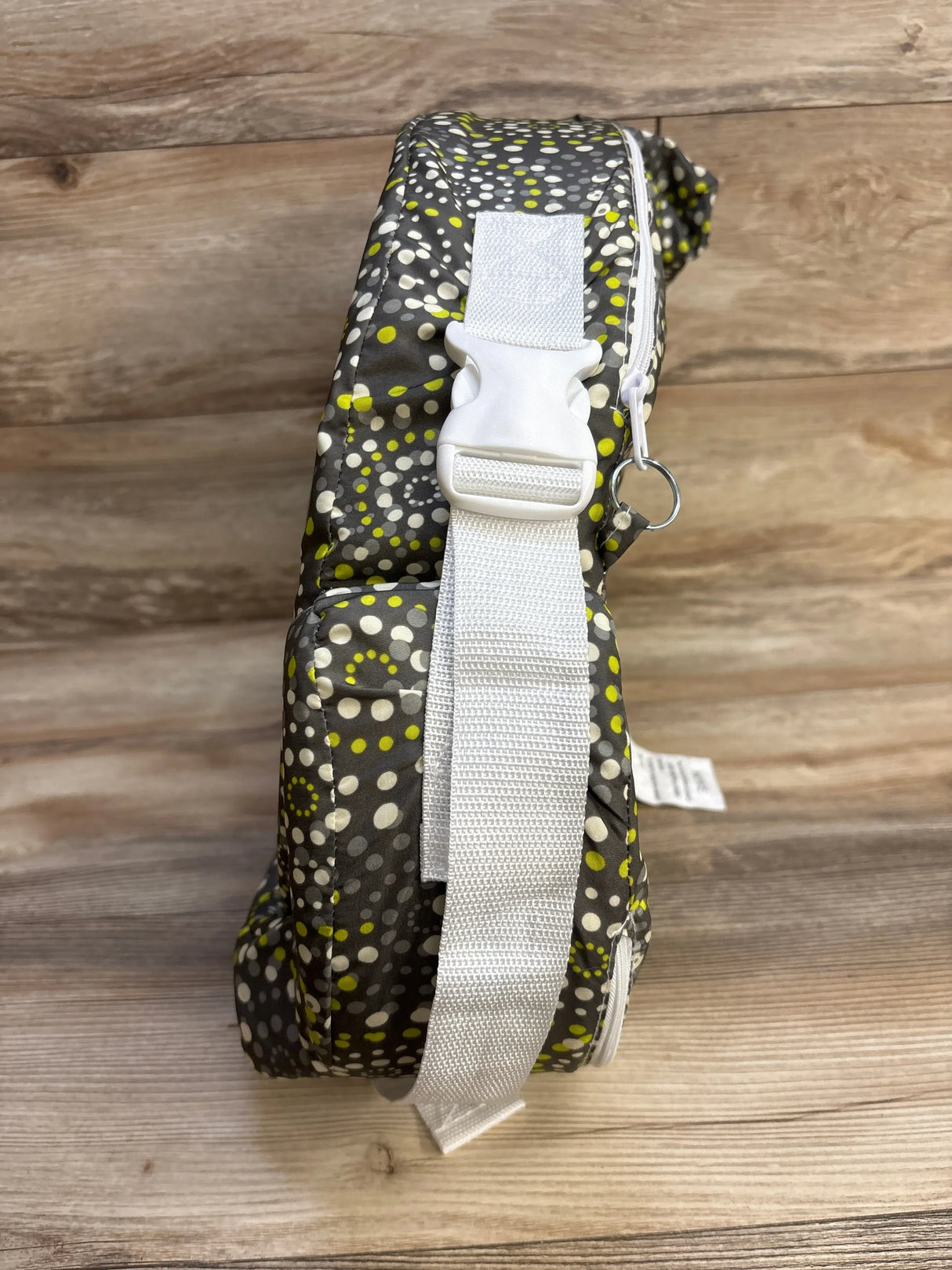 Side view of My Brest Friend nursing pillow in Fireworks pattern showing white adjustable strap and buckle on wood background