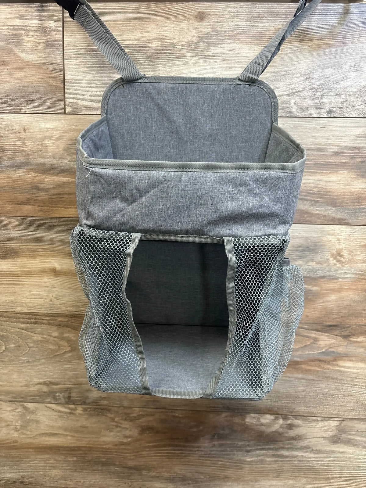 Front view of Maliton hanging diaper caddy with open main compartment and mesh side pockets on wood background