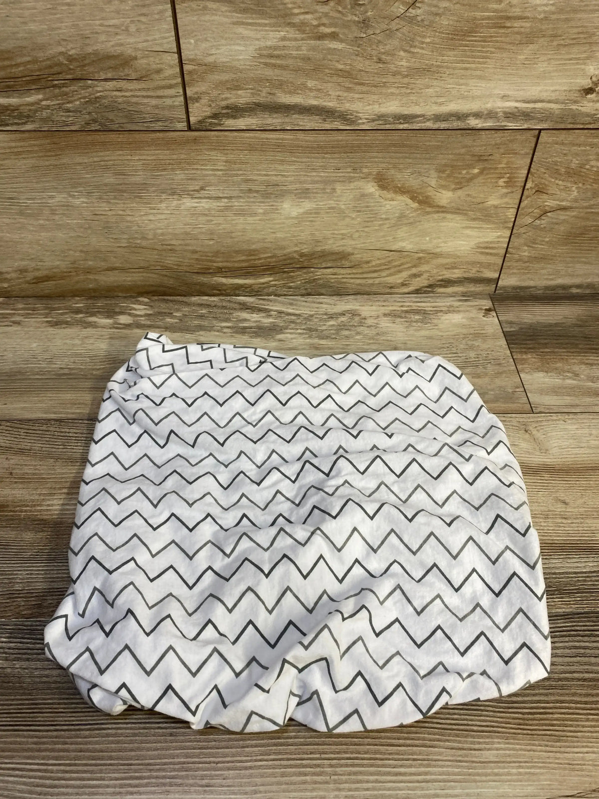 Top-down view of TL Baby fitted bassinet sheet showing gray chevron pattern and elastic edge on wood background