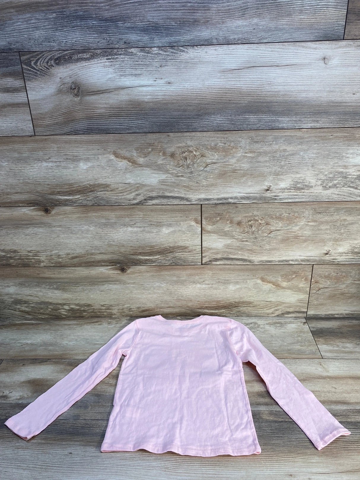 Light pink long sleeve kids shirt laid flat on wooden floor background