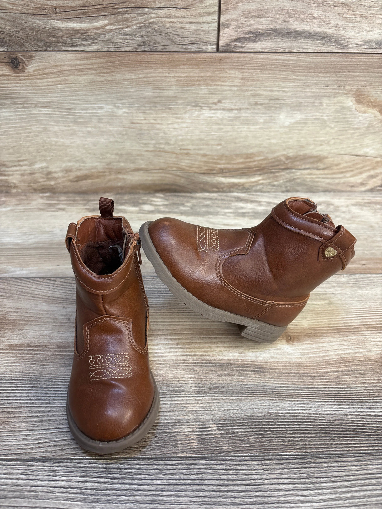 Pair of brown toddler ankle boots with decorative stitching on wooden floor