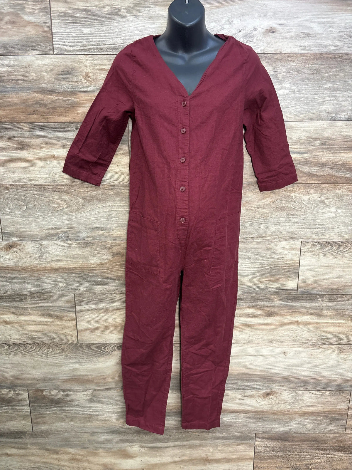 Wine red button-front maternity jumpsuit with 3/4 sleeves on a mannequin against a wood wall.