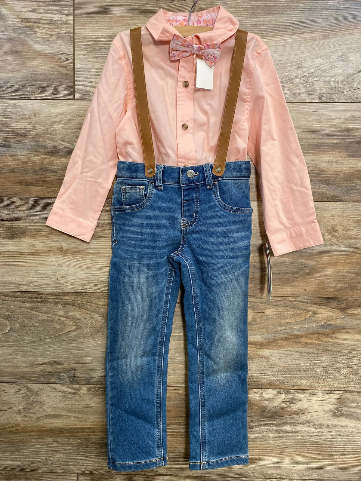 Front view of toddler suspender set with pink button-up shirt, floral bow tie, blue jeans and brown suspenders on wood floor