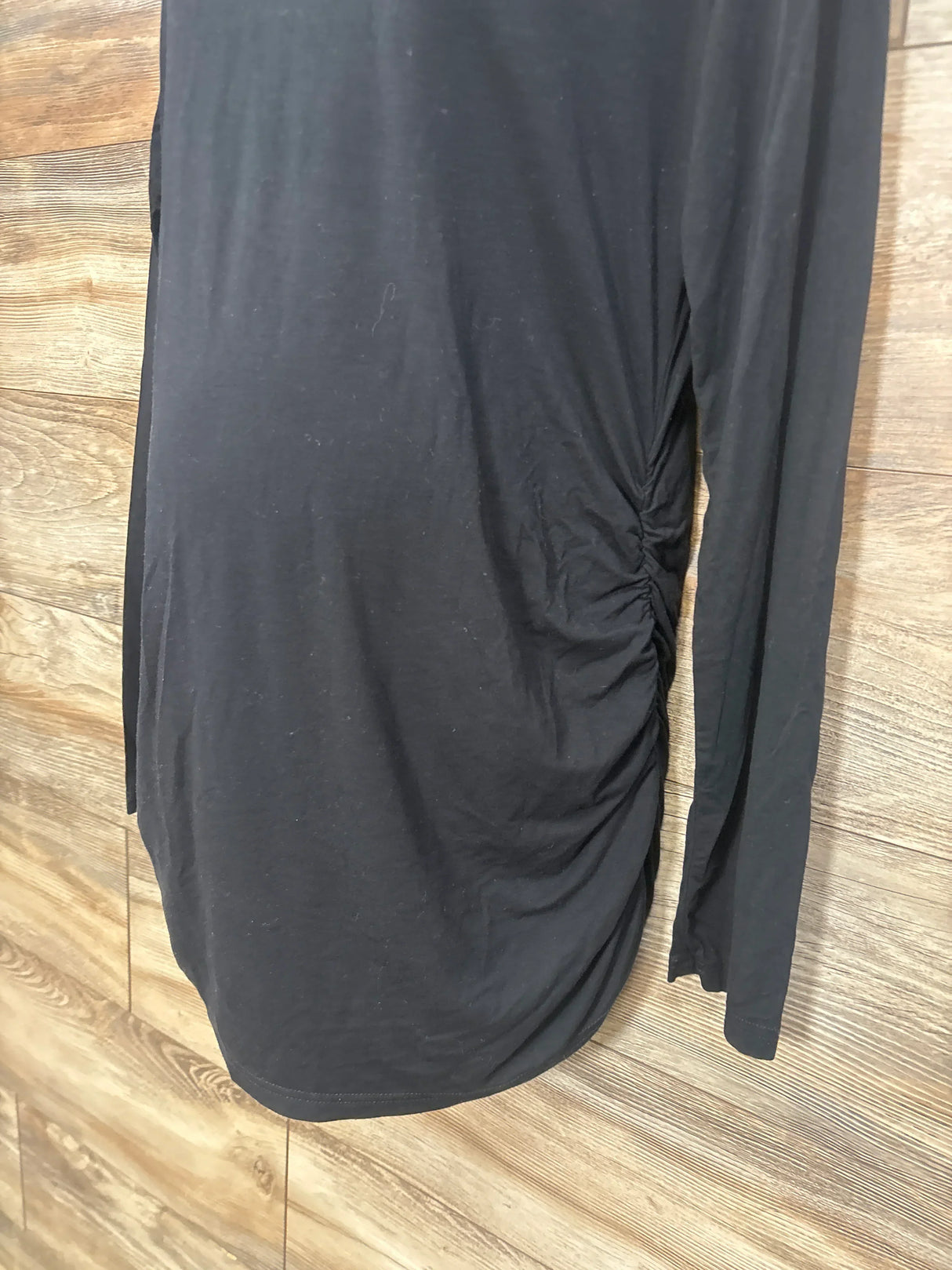 Black maternity dress with side ruching, long sleeves, laid on wood floor