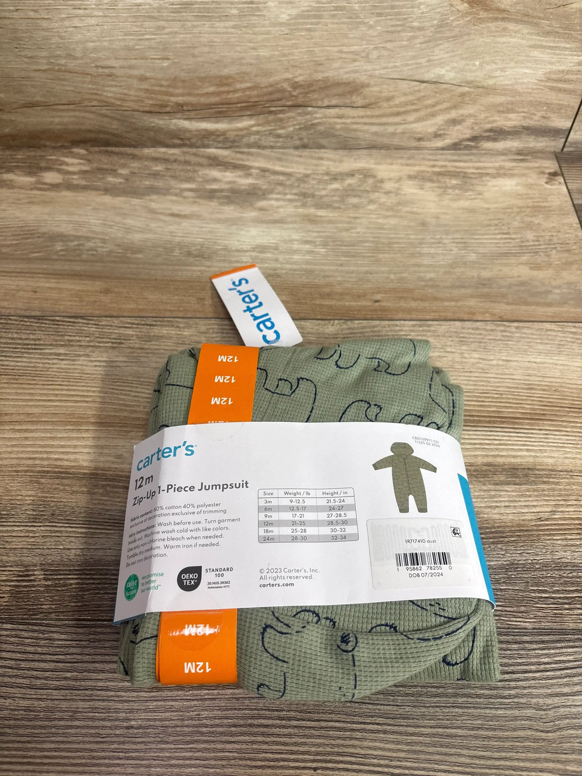 Top down view of Carter’s green waffle knit hooded coverall folded, showing animal outline print and 12M size tag on wooden background