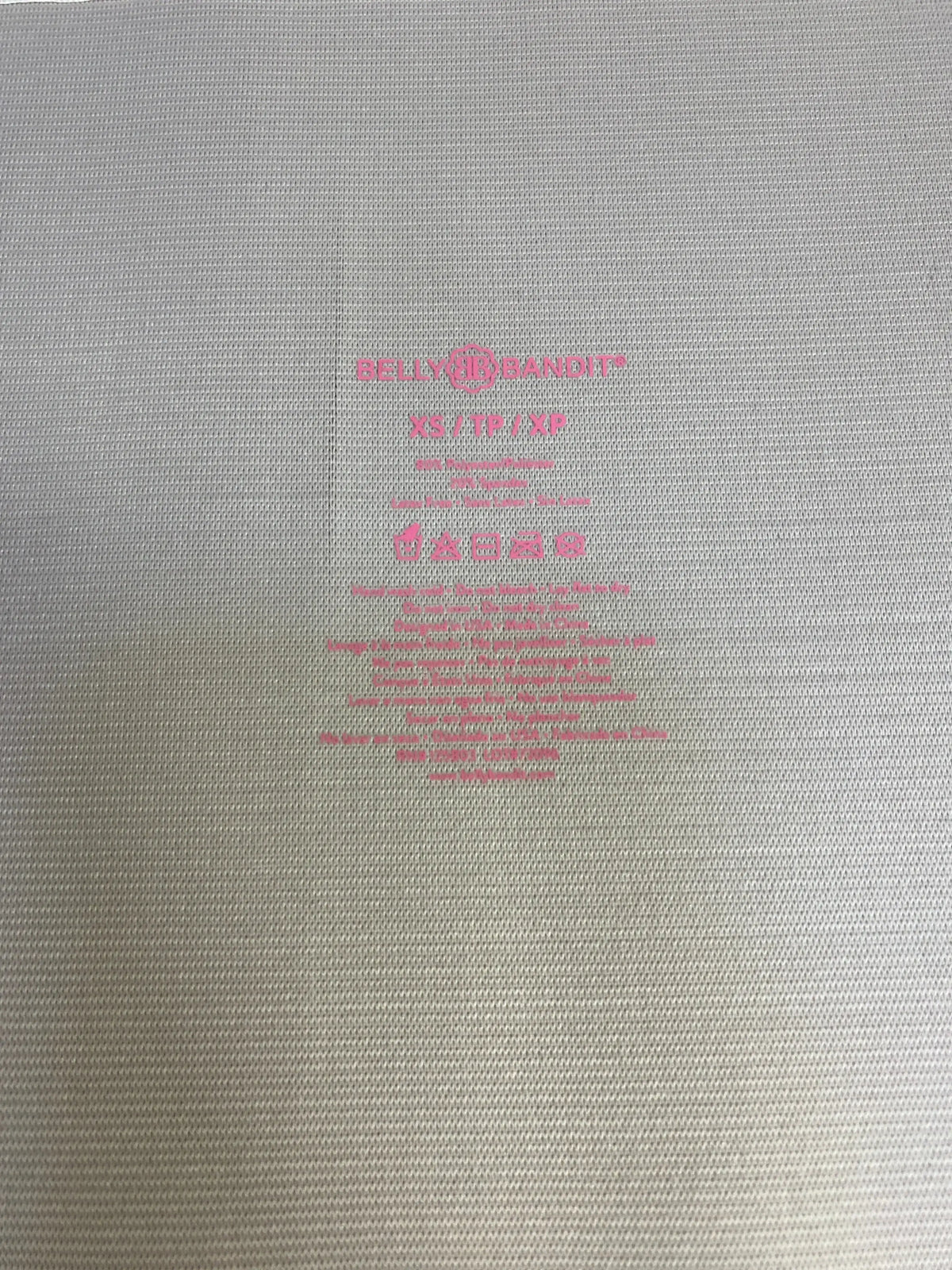 Close-up of Belly Bandit Postpartum Belly Wrap size XS in beige fabric with pink brand label and care instructions printed inside