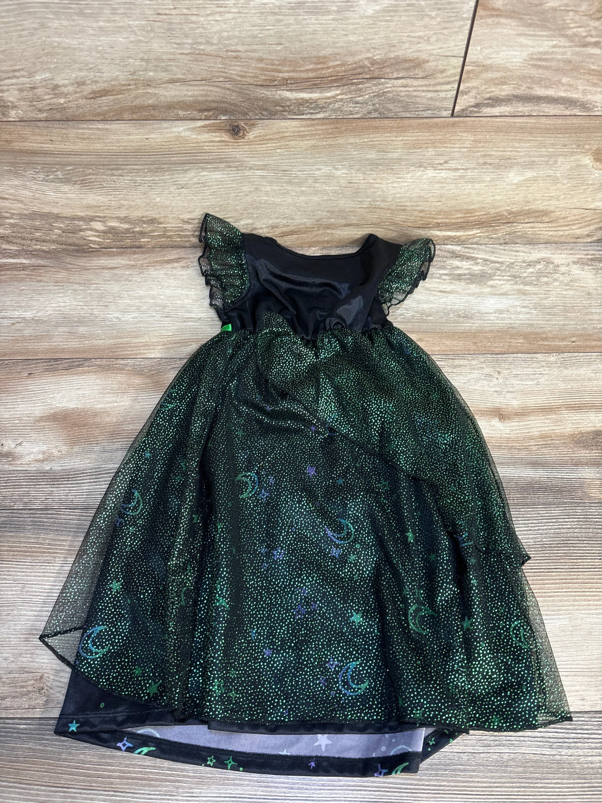 Flat lay of Wicked Elphaba toddler nightgown showing black bodice, green sparkly tulle skirt with moon and star print and ruffle cap sleeves on wood floor