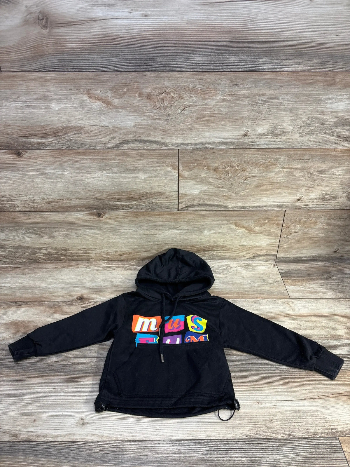 Black kids hoodie with colorful 'museum' graphic on wood floor background