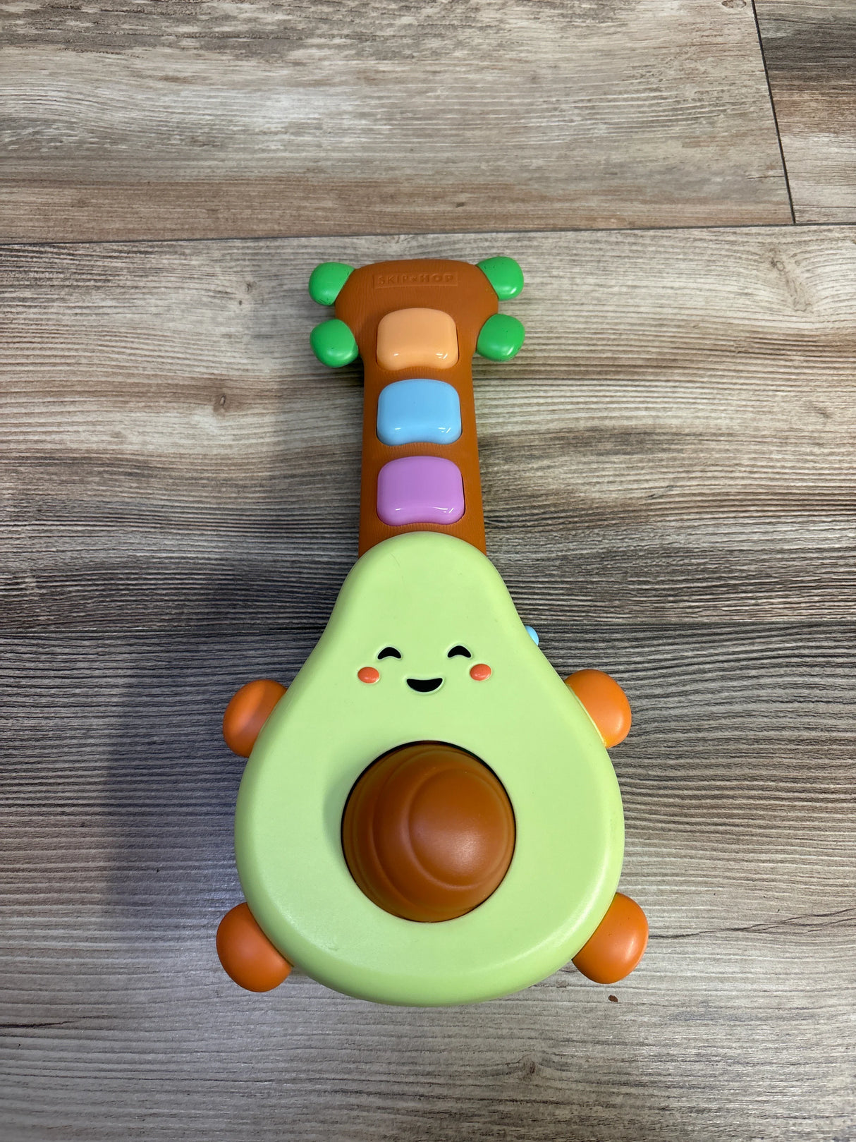 Me n Mommy To Be children's avocado-shaped toy guitar with smiling face and colorful buttons on wooden floor