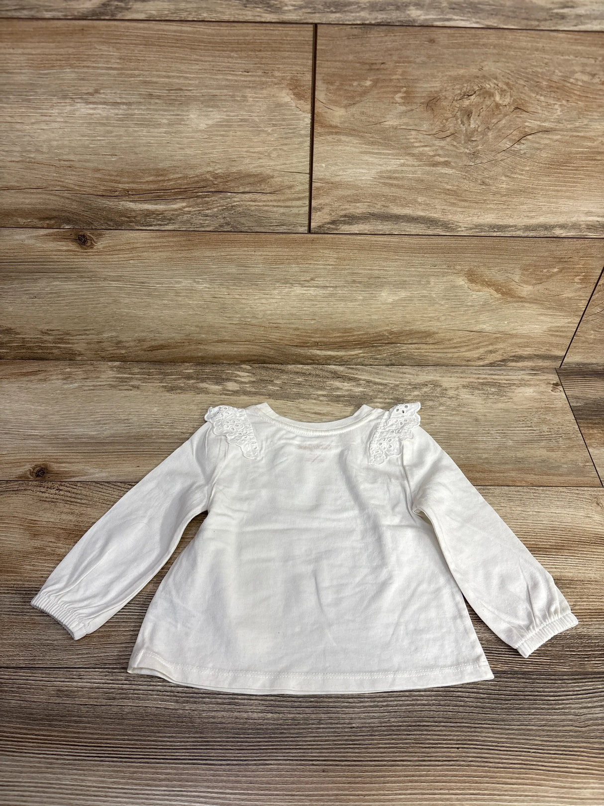 White long sleeve baby shirt with lace shoulder detail on wooden background