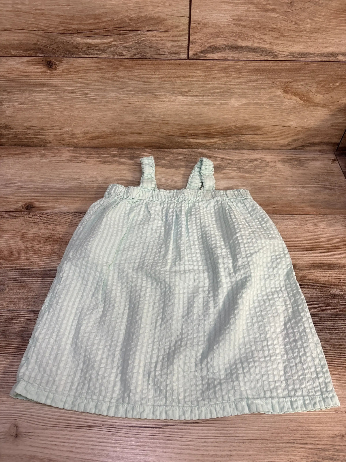 Top-down view of mint H&M toddler sleeveless textured dress with ruched elastic straps on wood background