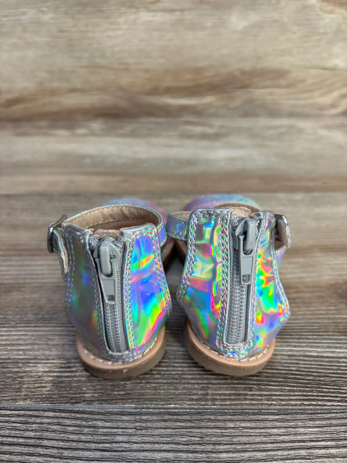 Rear view of Seychelles metallic sandals (size 5C) showcasing back zippers and holographic iridescent finish on wooden plank background