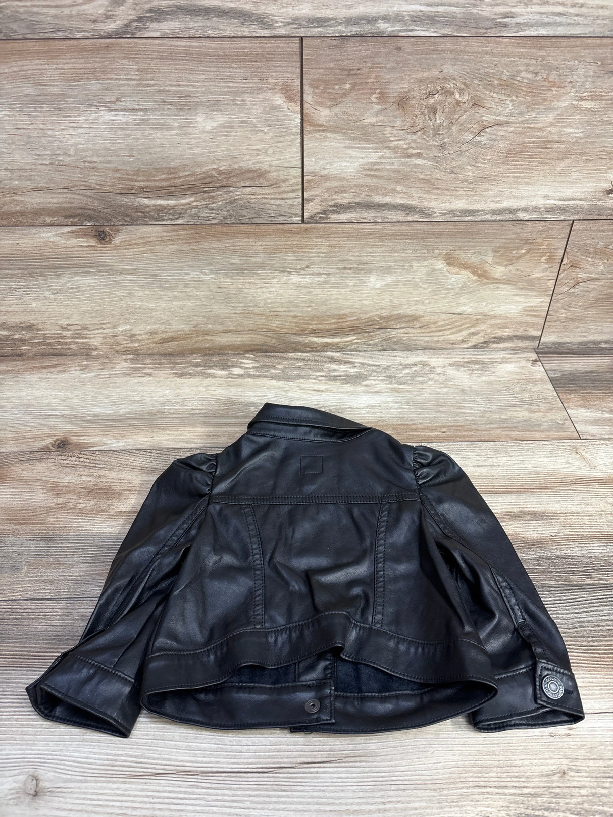 Back view of black faux leather jacket with puffed sleeves on wooden floor