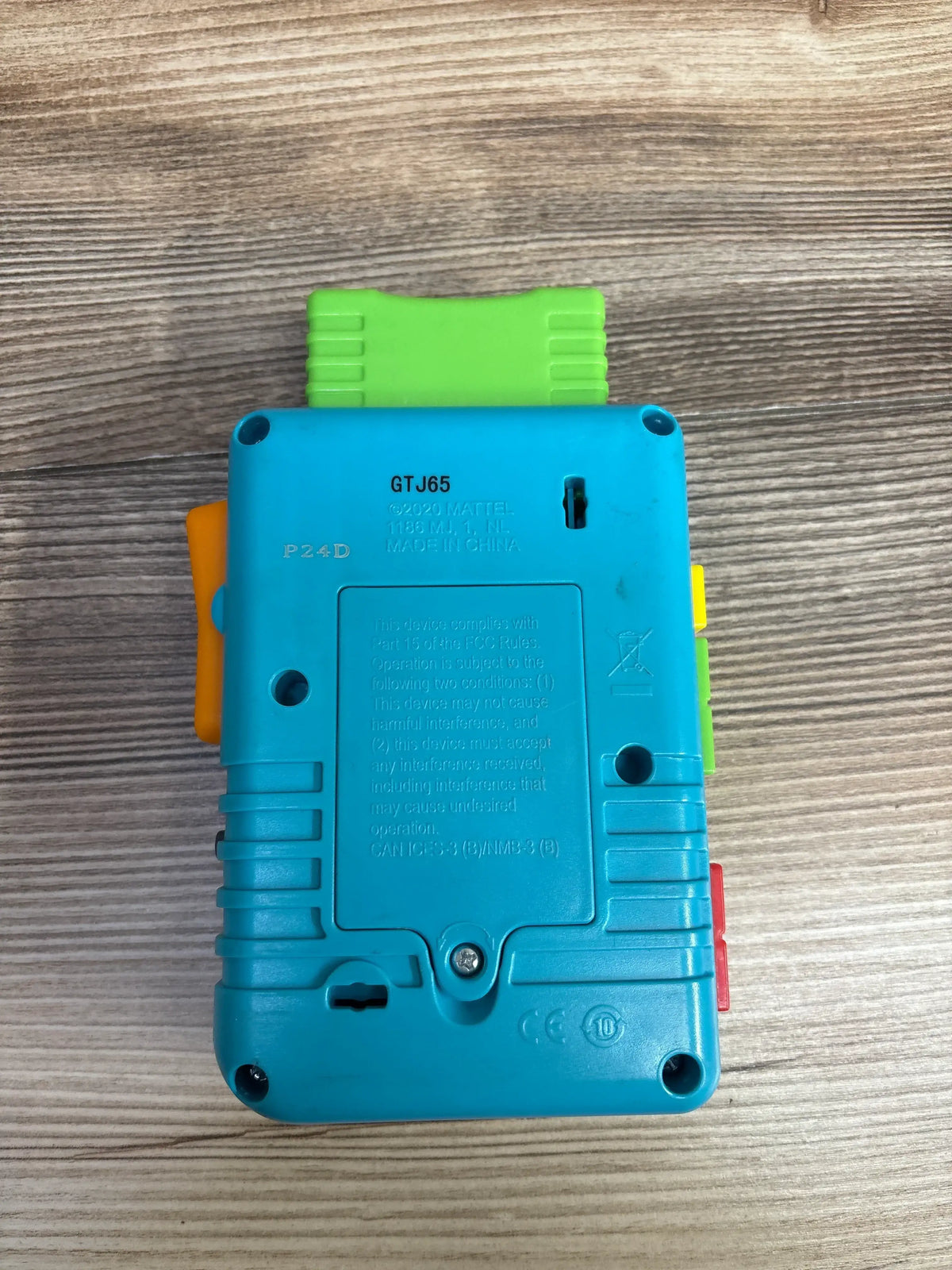 Back view of Fisher-Price Laugh & Learn Lil' Gamer showing battery compartment, screw and colored side buttons on a wood surface