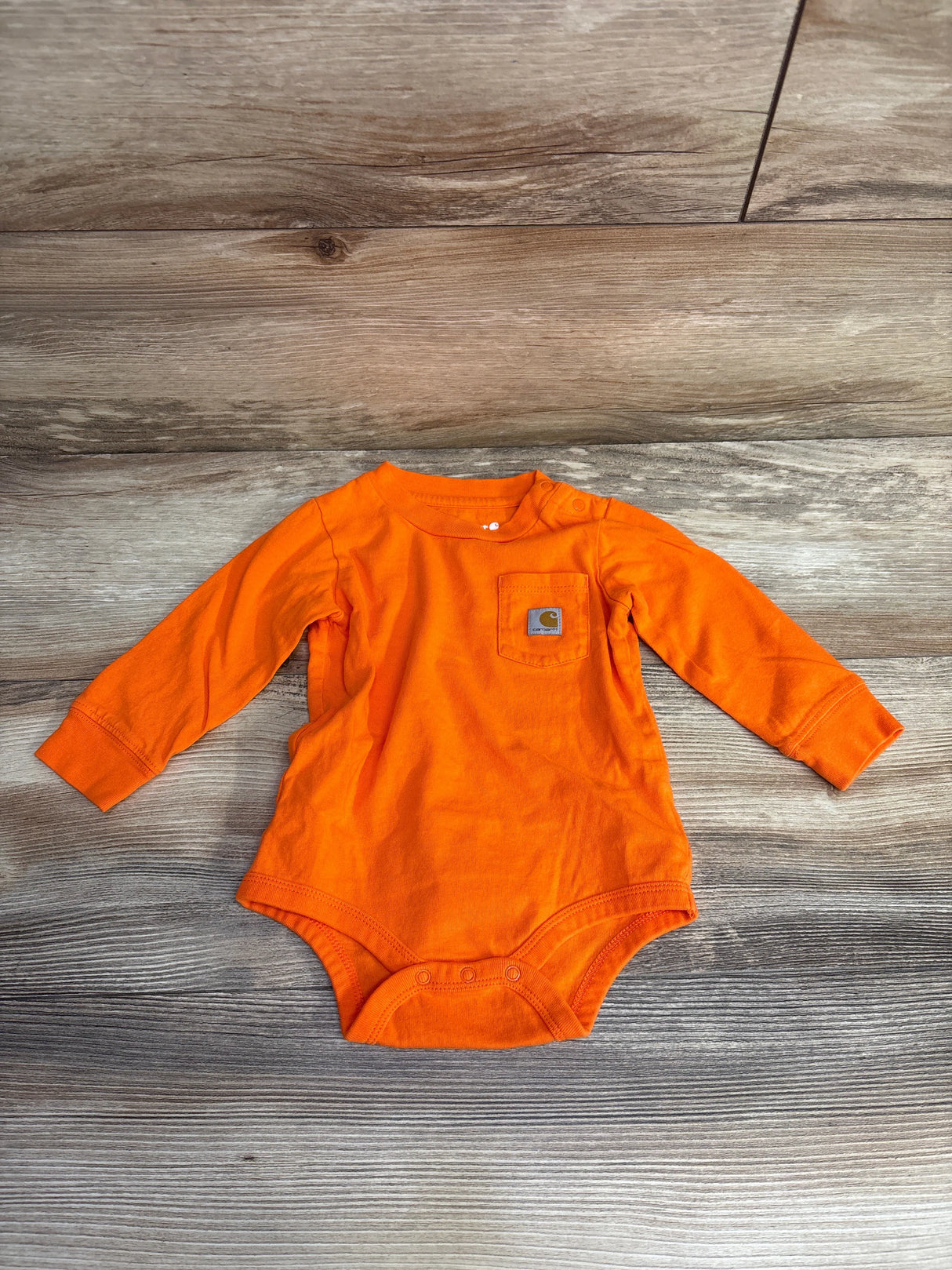 Bright orange long-sleeve baby onesie with front pocket on wooden floor