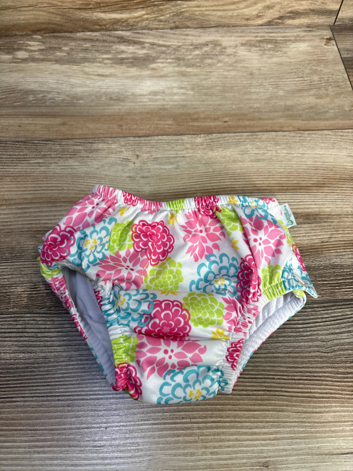 Front view of Green Sprouts floral white swim diaper, size 24 months, with floral pattern and elasticized openings on wood