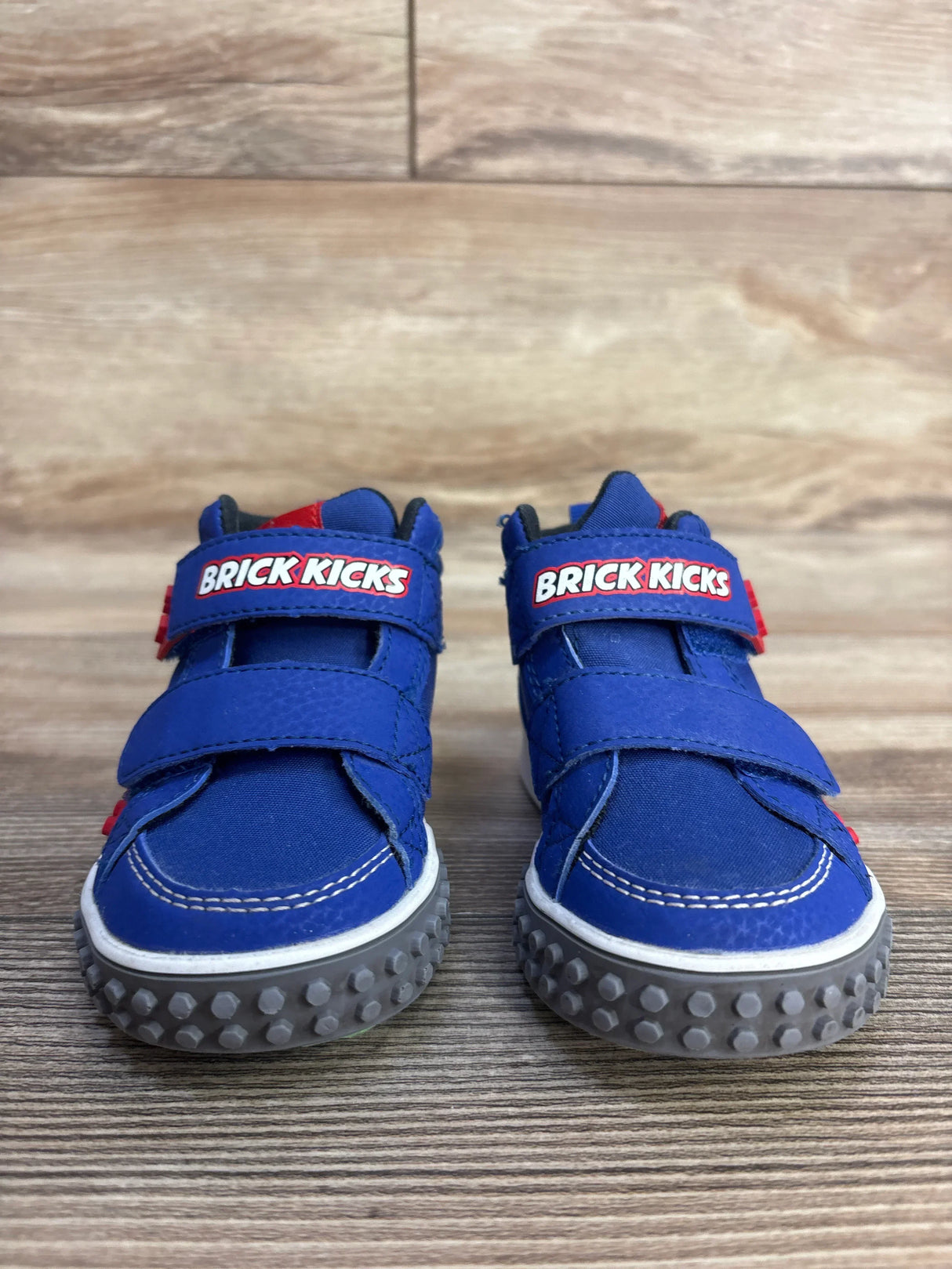 Front view of Skechers Kool Brick sneakers in blue showing BRICK KICKS velcro straps and grey studded soles on wood floor