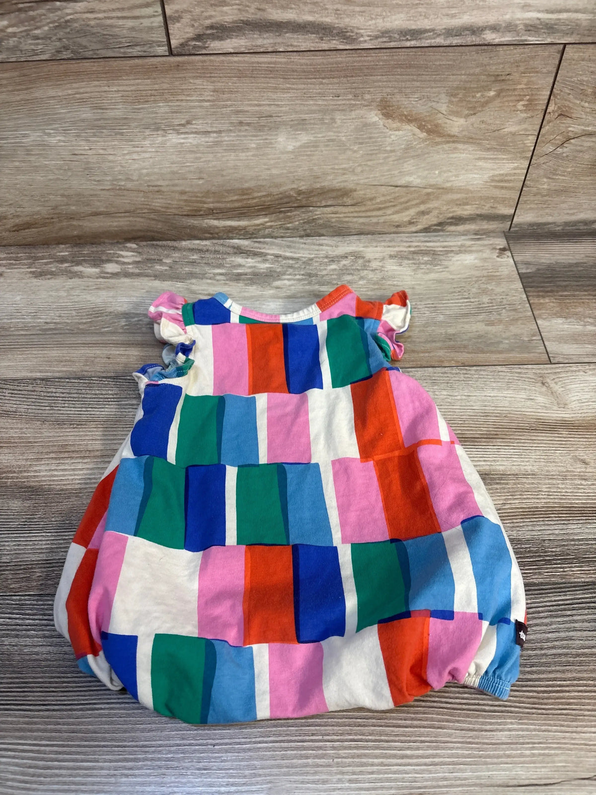 Colorful patchwork baby romper with ruffled sleeves on wooden floor