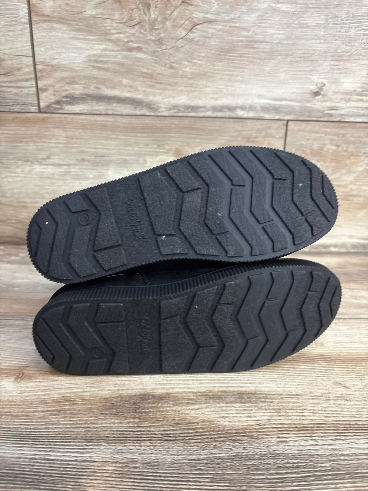 Pair of black children's shoes showing textured soles on a wooden floor, resale kids footwear