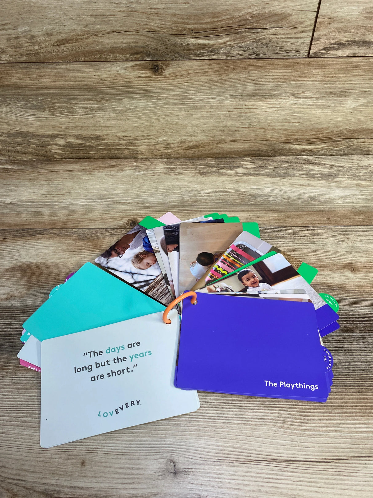 Lovevery baby plaything cards fanned out on wood surface, featuring quotes and baby images