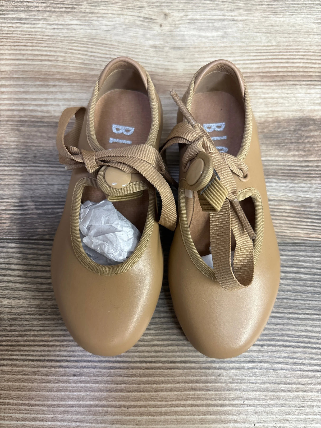 Top view of Bloch Annie Tyette tan toddler tap shoes showcasing ribbon tie straps and round toes on a wood floor