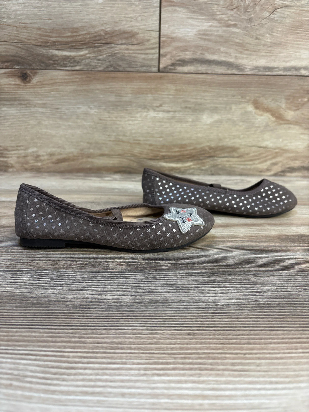 Girls brown flat shoes with silver star patterns and embroidered star accent, wooden background