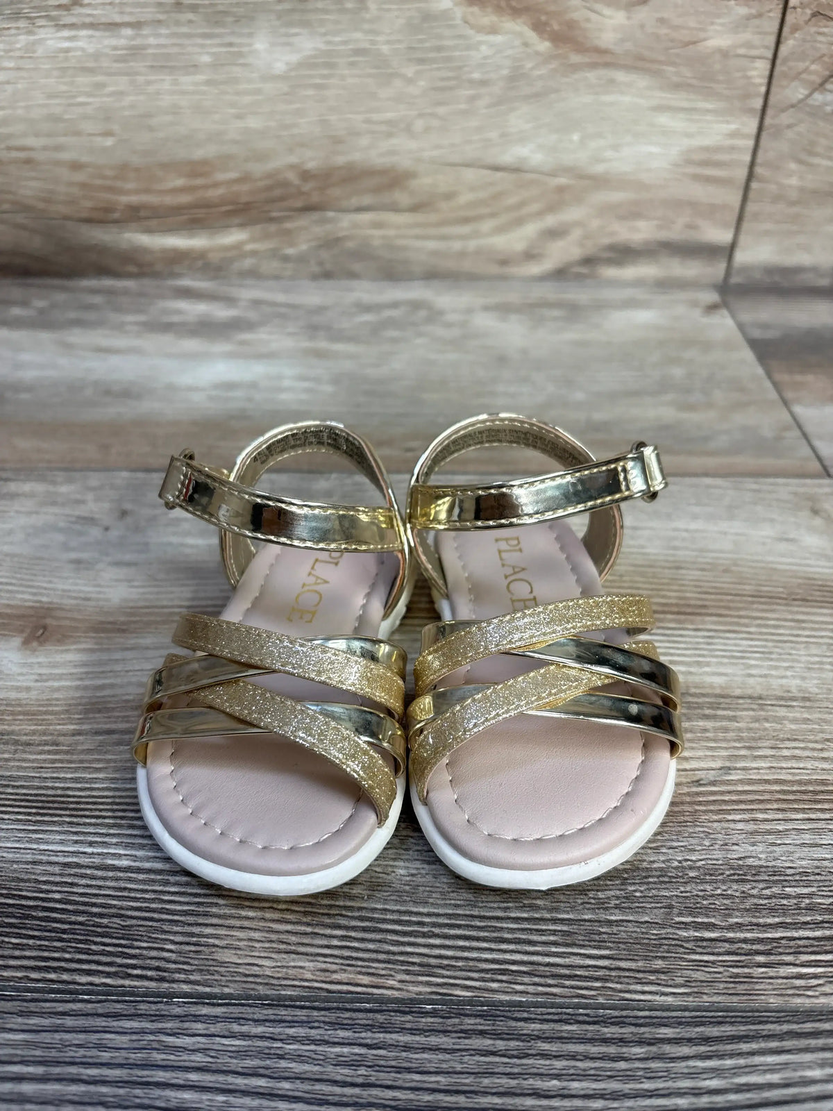 Children's Place gold glitter and metallic sandals for toddlers on a wooden surface