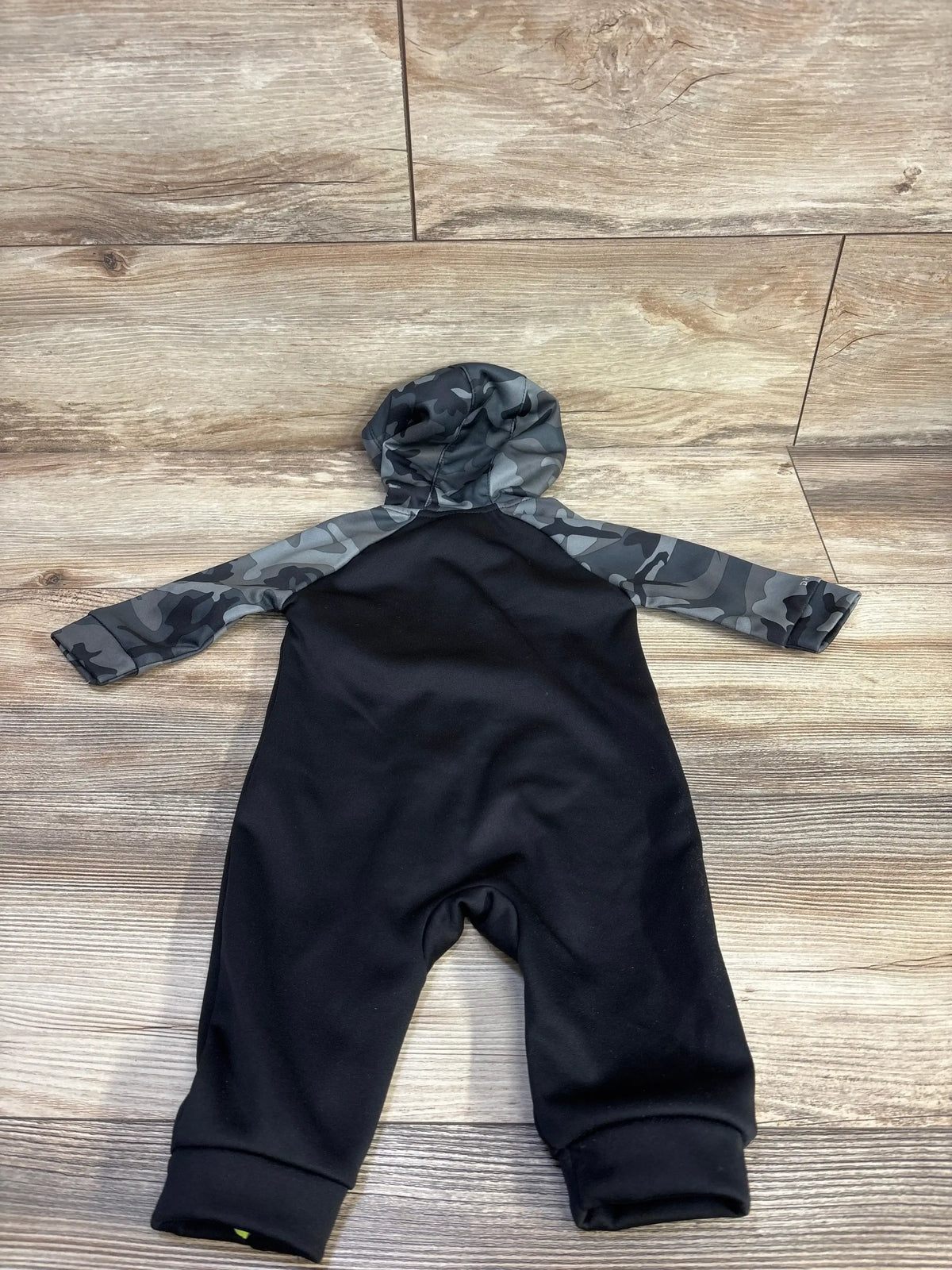 Flat lay of Nike Dri-Fit hooded coverall, black body with gray camo sleeves and hood, cuffed ankles on wood background