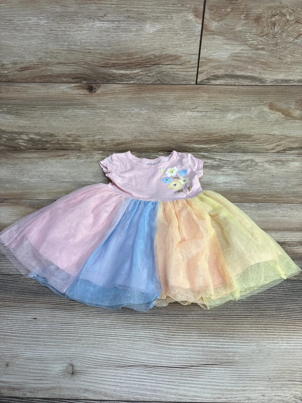 Top-down view of Carter's pink 18m dress showcasing embroidered floral bodice and pastel rainbow tulle skirt on wood floor