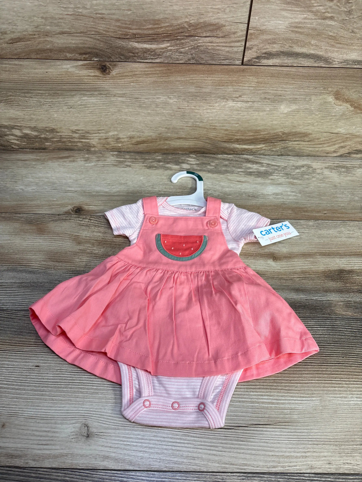 Front view of Just One You two piece pink skirtall and bodysuit set with watermelon applique on wood background