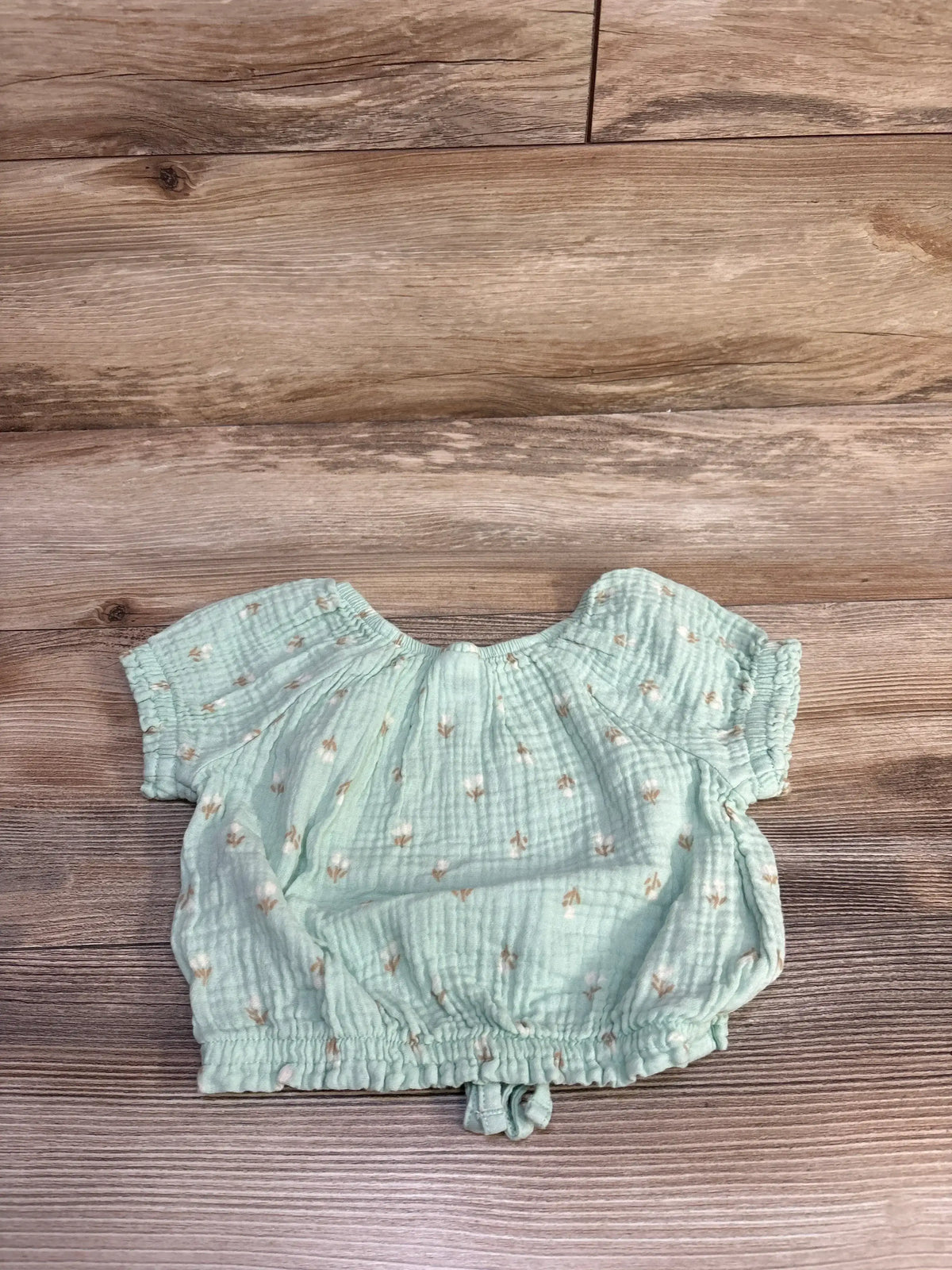 Flat lay of Member’s Mark toddler gauze shirt in mint green with small tan floral print, crinkled fabric and elastic hem on wood background