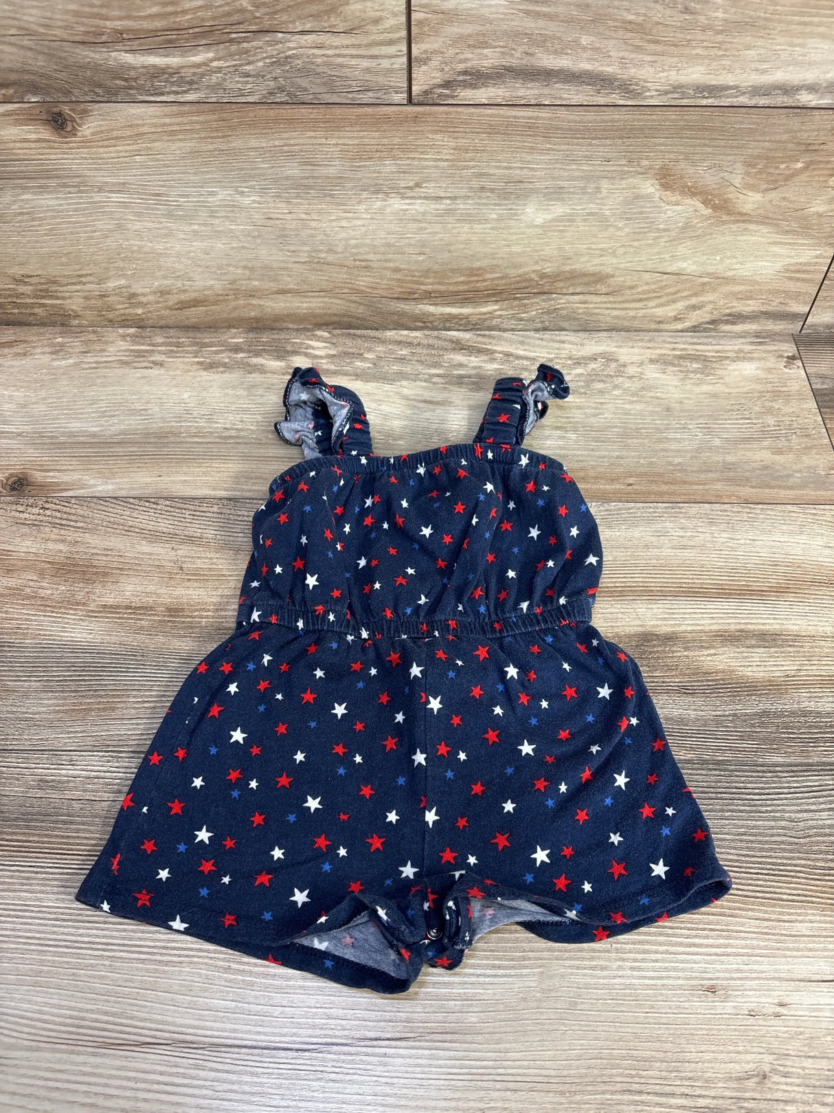 Flat lay of navy Old Navy sleeveless baby romper showcasing red, white, and blue star print and snap crotch on wood floor