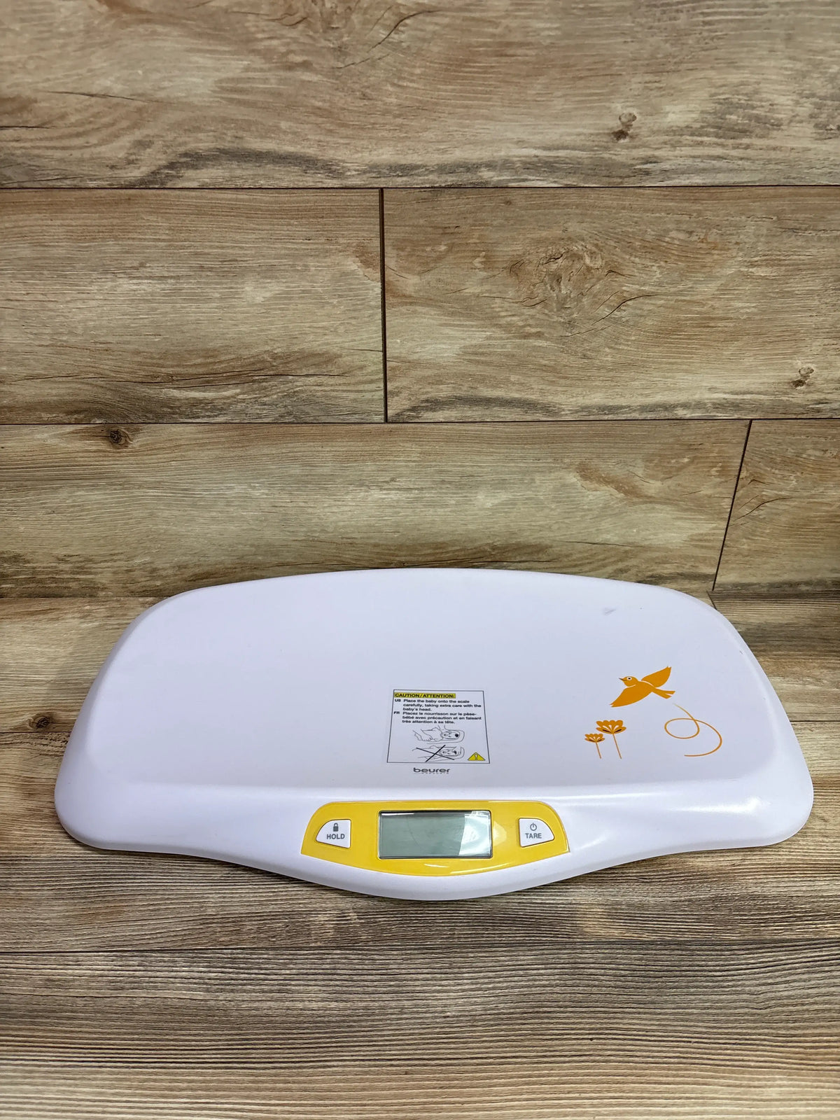 Front view of Beurer BY80 digital baby scale showcasing white platform, yellow control panel, HOLD and TARE buttons on a wood surface