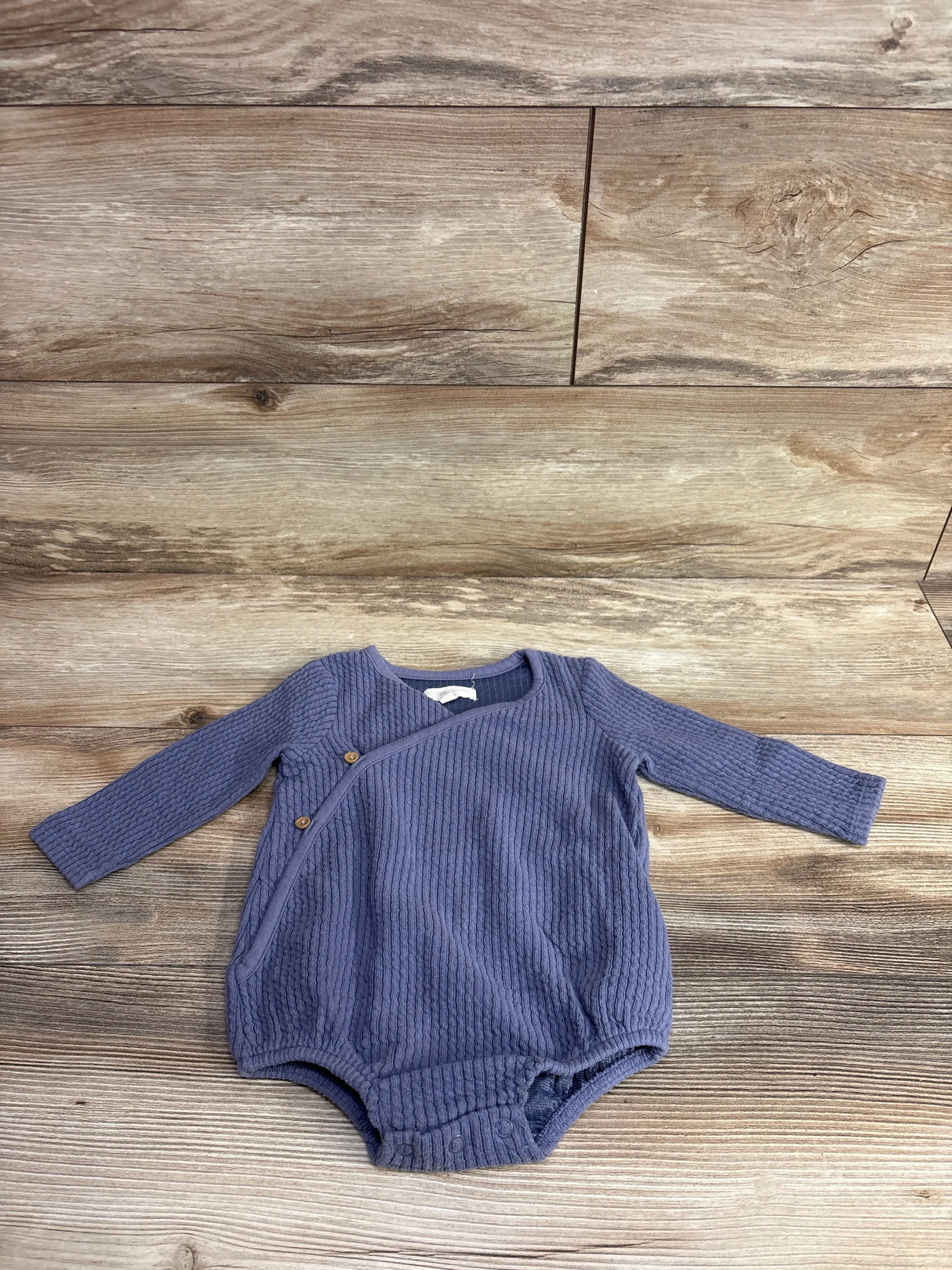 Blue ribbed long-sleeve baby onesie with snap buttons on wooden background, kids clothes resale